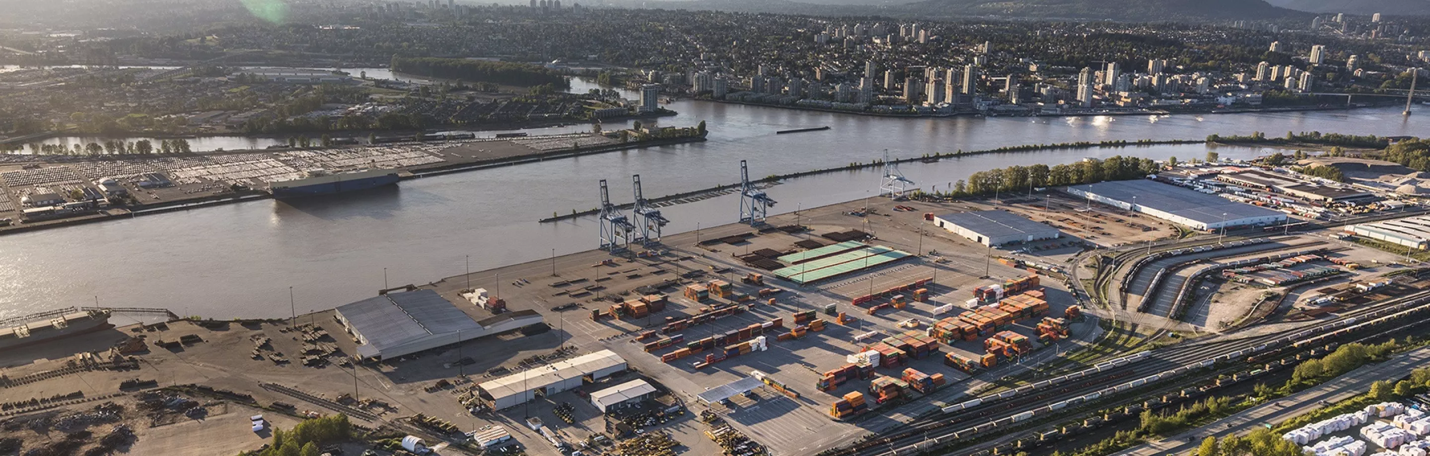 L'image est traversée horizontalement par un fleuve. Une ville et des montagnes sont visibles sur la rive supérieure et un terminal portuaire se trouve sur la rive inférieure.