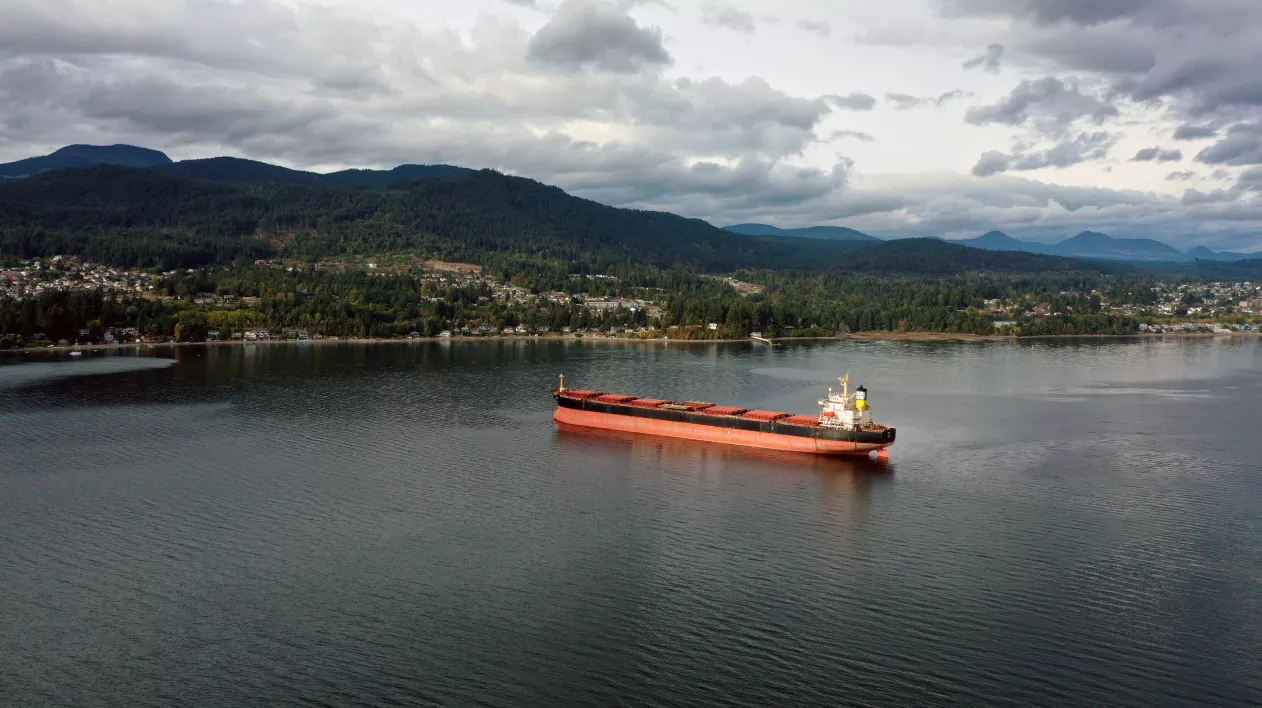 A orange cargo ship floats in Burrard Inlet