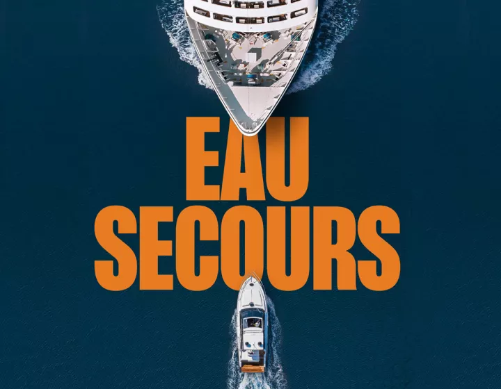 Bannière de campagne - Eau Secours Une bannière promotionnelle montre deux bateaux naviguant sur un océan bleu profond, l'un grand et l'autre plus petit, se dirigeant l'un vers l'autre depuis des directions opposées. Le grand texte "EAU SECOURS" est placé en lettres majuscules orange entre les deux navires. La perspective est vue d'en haut, mettant en évidence la différence de taille entre les bateaux.